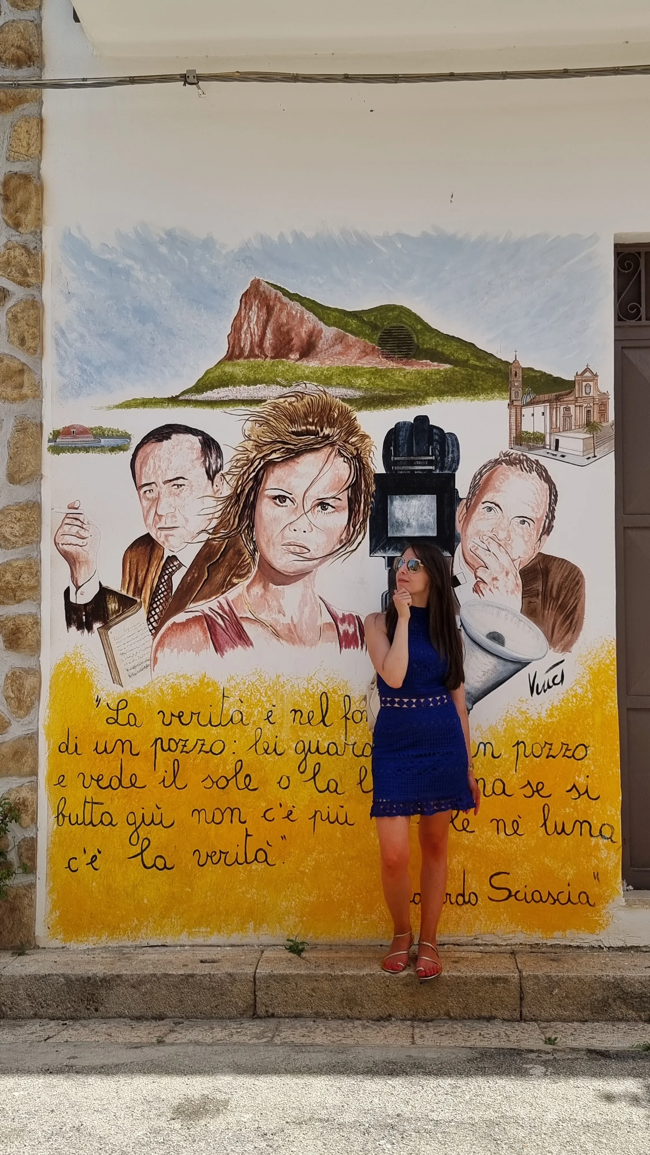 Deena in a blue dress in front of a painted Sicilian mural.
