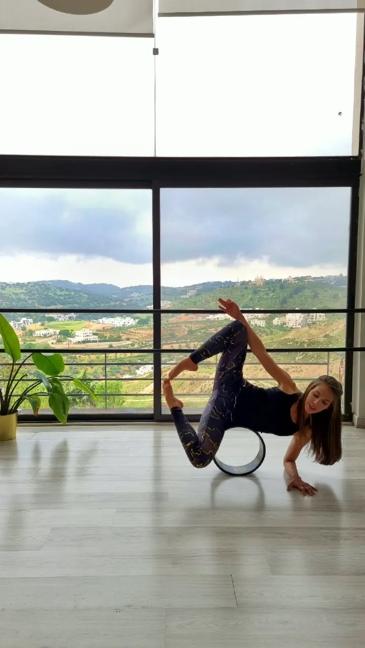 Deena balancing on a yoga wheel in a bright room, the hills of Amman through the window behind her.